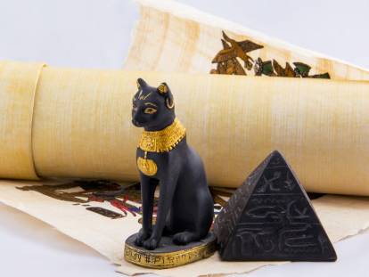 Une statue d'un chat noir égyptien, des papyrus et une pyramide.