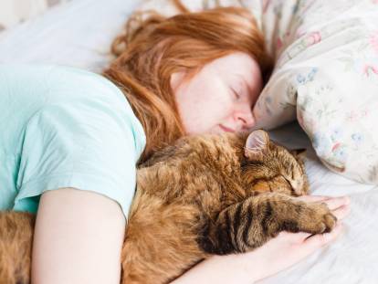 Une femme rousse dort avec son chat dans son lit