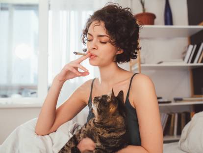 Une femme fume dans sa chambre à côté de son chat
