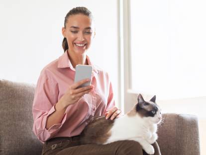 Une femme assise sur un canapé qui regarde son téléphone avec un chat couché sur ses genoux