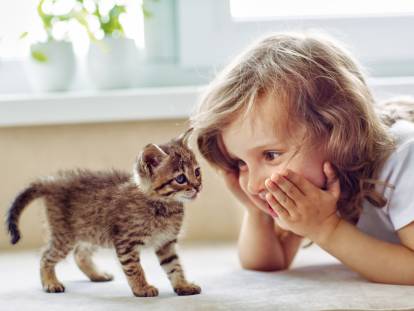 Une enfant allongée par terre regardant un chaton