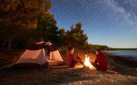 Un couple de campeurs assis devant un feu sous un ciel étoilé