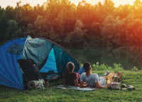 Un couple allongé sur l'herbe à côté d'une tente admire le coucher de soleil sur un lac
