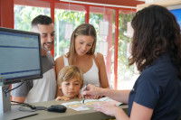 Une réceptionniste présente la carte de leur lieu de vacances à un couple et leur enfant