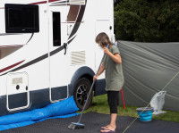 Une femme en train de nettoyer un tapis devant un camping-car