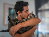 Un homme tenant un chat dans ses bras et lui faisant un bisou