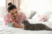 Une femme allongée sur un lit, à côté de son chat, passant un appel téléphonique
