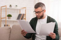 Un homme assis sur un canapé et en train de lire différents documents.