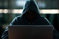 Un homme dissimulé sous sa capuche, derrière un ordinateur portable