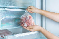 Une femme place un sachet de viande au congélateur