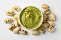 Des pistaches entières et du beurre de pistache sur un fond gris