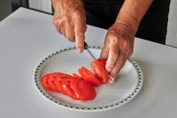 Un homme coupe une tomate dans une assiette