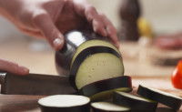 Une femme découpe une aubergine en tranches