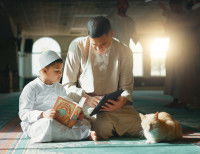 Un chat couché à l'intérieur d'une mosquée, devant un homme et un enfant en train d'étudier le Coran