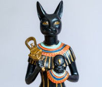 Une statue de la déesse Bastet (avec un corps de femme et une tête de chat), tenant plusieurs objets dans ses mains.