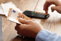 Une personne tenant des billets et en train de taper sur une calculatrice