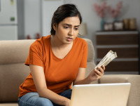 Une femme tenant des billets et faisant ses comptes sur son ordinateur