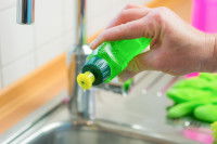 Une femme verse du liquide vaisselle dans un évier