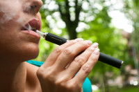 Une femme fume une cigarette électronique dans un parc