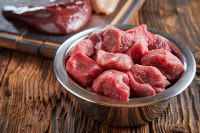 Une gamelle contenant de la viande crue sur une table en bois