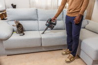 Un homme passe l'aspirateur sur le canapé où son chat est assis