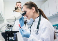 Une scientifique regarde dans son microscope pendant qu'un autre tient un chat en arrière-plan