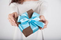 Une femme tend un cadeau brun avec un ruban bleu