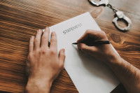 Une personne en train d'écrire une déclaration sur une feuille de papier, avec des menottes à côté