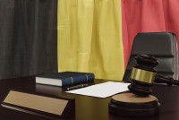 Un livre de droit et un maillet posés sur un bureau devant le drapeau belge