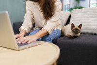 Une femme assise sur un canapé, qui semble accaparée par son ordinateur et ignorer son chat.