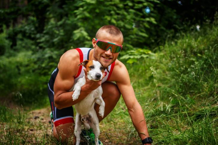 Un Jack Russell tenu par un sportif dans une forêt