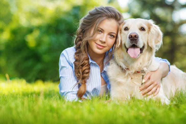Un Golden Retriever allongé dans l'herbe et enlacé par sa propriétaire 