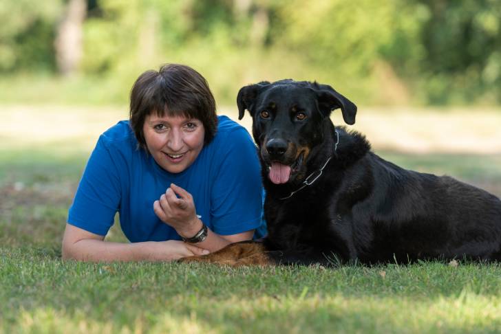 Un Beauceron allongé dans l'herbe à côté de sa propriétaire 