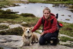 Un Welsh Corgi Pembroke allong&eacute; sur une montagne &agrave; c&ocirc;t&eacute; d'une femme accroupie et portant un sac au dos 